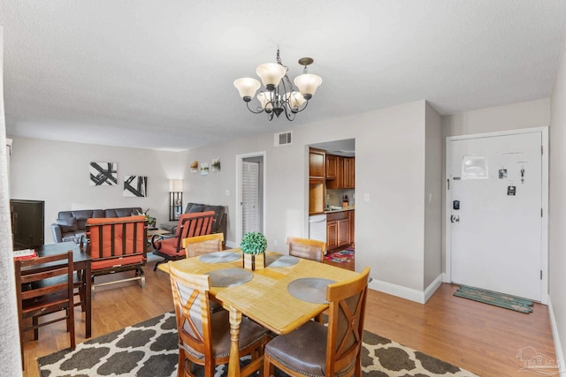 dining area with light wood-style floors, a chandelier, visible vents, and baseboards