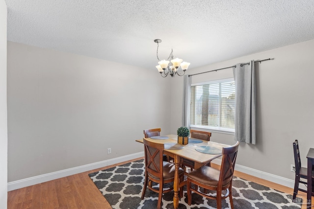 dining area featuring a chandelier, a textured ceiling, wood finished floors, and baseboards