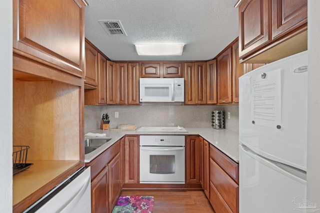 kitchen with light wood-style flooring, white appliances, visible vents, light countertops, and brown cabinets