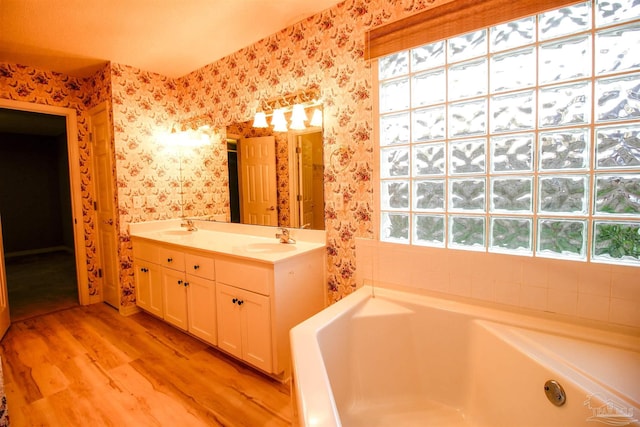 full bathroom with wallpapered walls, wood finished floors, a garden tub, and double vanity