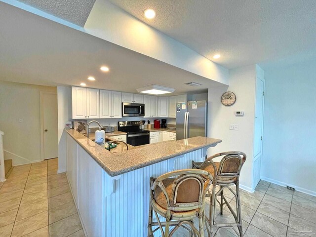 kitchen with appliances with stainless steel finishes, white cabinetry, kitchen peninsula, a textured ceiling, and a kitchen bar