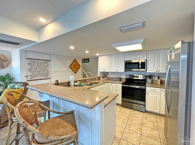 kitchen featuring a kitchen breakfast bar, white cabinetry, kitchen peninsula, stainless steel appliances, and sink