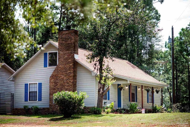 view of front of property featuring covered porch, a shingled roof, a chimney, and a front yard