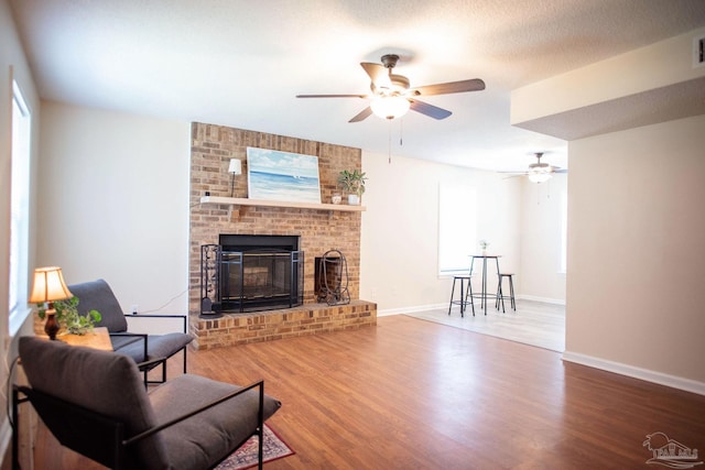 living area featuring wood finished floors, a ceiling fan, visible vents, baseboards, and a brick fireplace