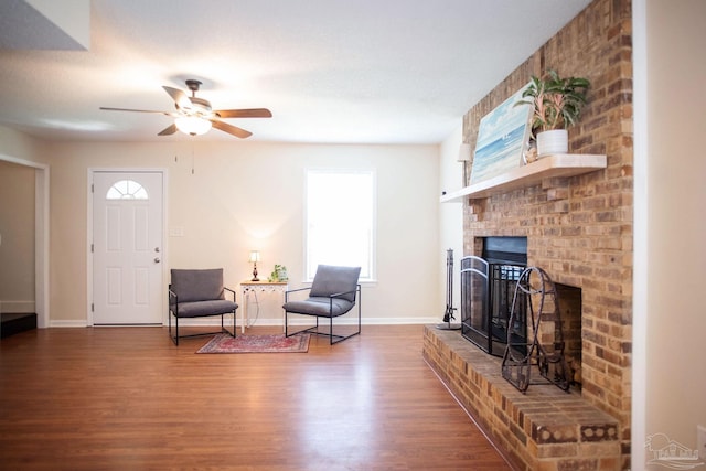 interior space featuring a brick fireplace, wood finished floors, a ceiling fan, and baseboards