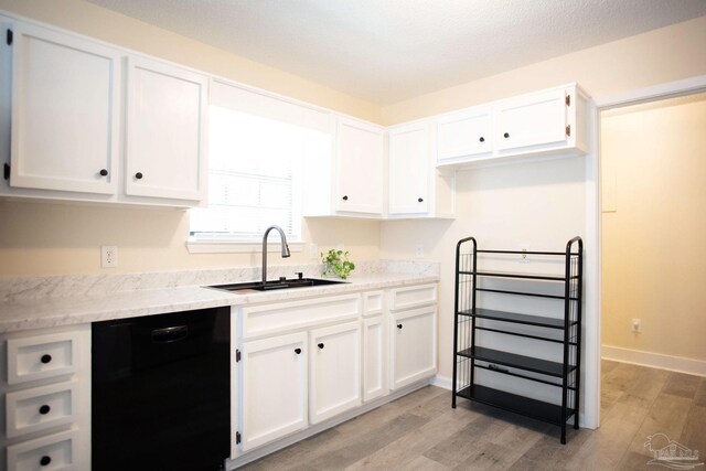 kitchen with black dishwasher, white cabinetry, a sink, and light wood-style flooring