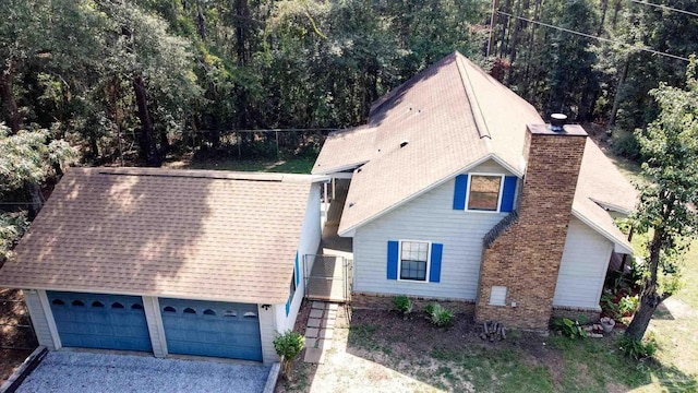 exterior space with a garage, a shingled roof, and a chimney