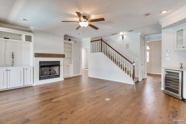 unfurnished living room featuring beverage cooler, visible vents, stairway, wood finished floors, and a fireplace