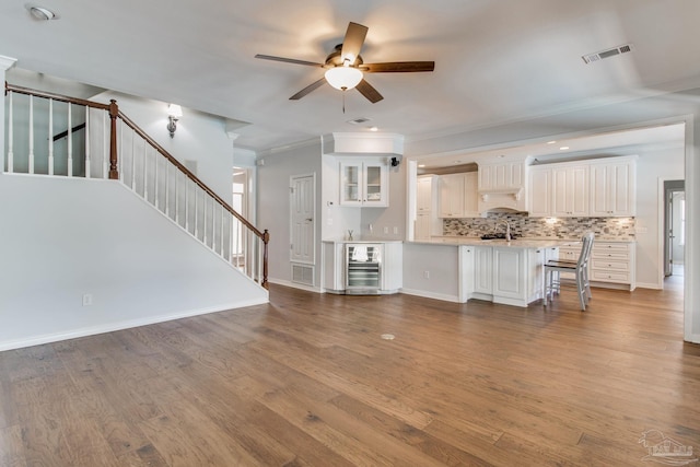 unfurnished living room with wine cooler, visible vents, stairway, and wood finished floors