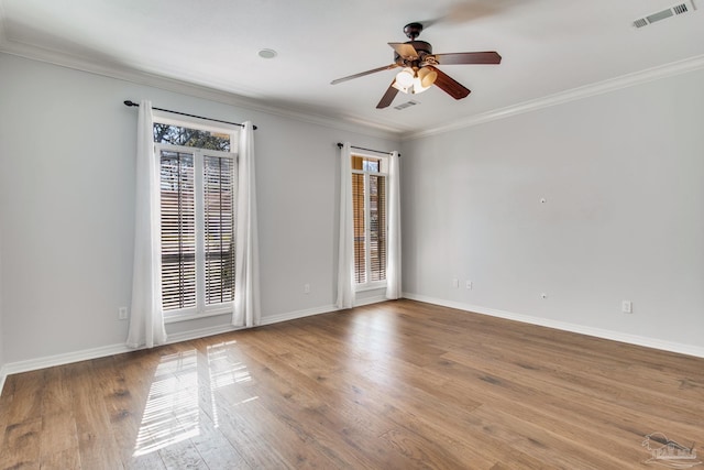 empty room with visible vents, ornamental molding, a ceiling fan, wood finished floors, and baseboards