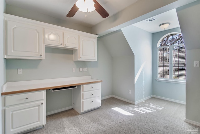 unfurnished office featuring ceiling fan, light colored carpet, visible vents, baseboards, and built in desk