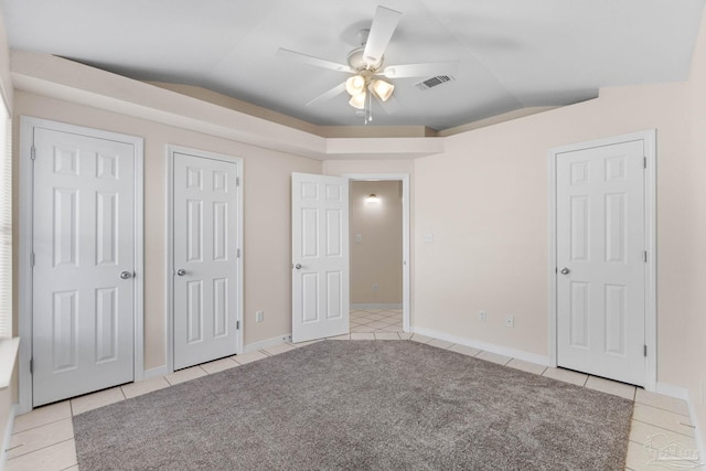 unfurnished bedroom with two closets, ceiling fan, light tile patterned flooring, and lofted ceiling