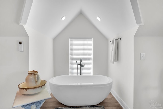 bathroom with wood-type flooring, vaulted ceiling, and a bathing tub