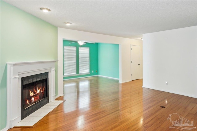 unfurnished living room featuring a fireplace, wood finished floors, a textured ceiling, and a ceiling fan
