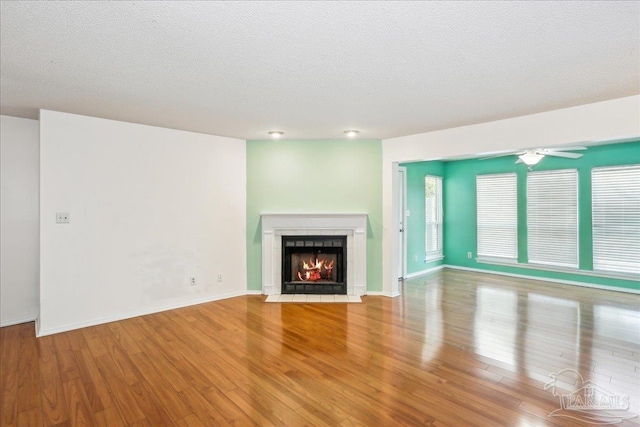 unfurnished living room with a fireplace with flush hearth, wood finished floors, a textured ceiling, and baseboards