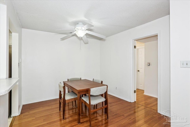 dining area featuring light wood-style floors, a textured ceiling, baseboards, and ceiling fan