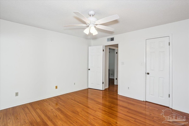 unfurnished bedroom featuring a textured ceiling, baseboards, visible vents, a ceiling fan, and wood finished floors
