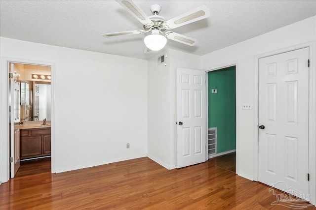 unfurnished bedroom featuring wood finished floors, ceiling fan, baseboards, ensuite bath, and visible vents