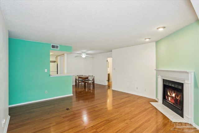 living area with a textured ceiling, a tiled fireplace, visible vents, wood finished floors, and ceiling fan