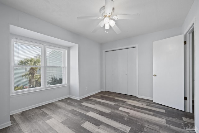 unfurnished bedroom with ceiling fan, a closet, dark wood-type flooring, and multiple windows