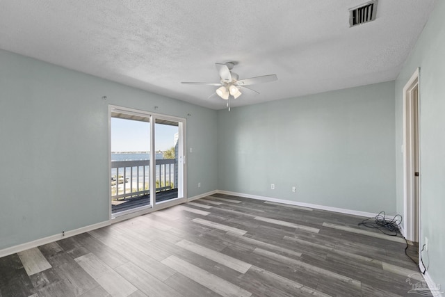 unfurnished room featuring a textured ceiling, dark hardwood / wood-style flooring, a water view, and ceiling fan