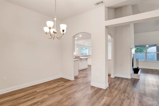 empty room with hardwood / wood-style flooring, a notable chandelier, a healthy amount of sunlight, and high vaulted ceiling