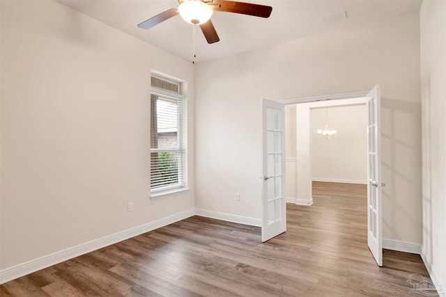 spare room featuring wood-type flooring and ceiling fan with notable chandelier