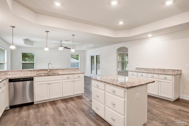 kitchen with a kitchen island with sink, a raised ceiling, sink, stainless steel dishwasher, and decorative light fixtures