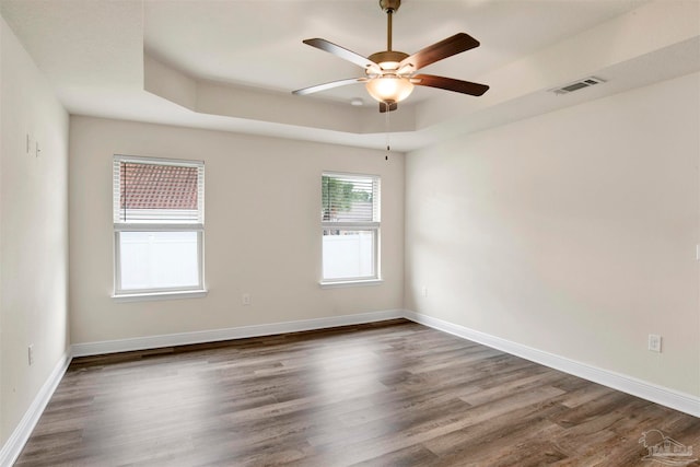 spare room with a raised ceiling, ceiling fan, and dark wood-type flooring