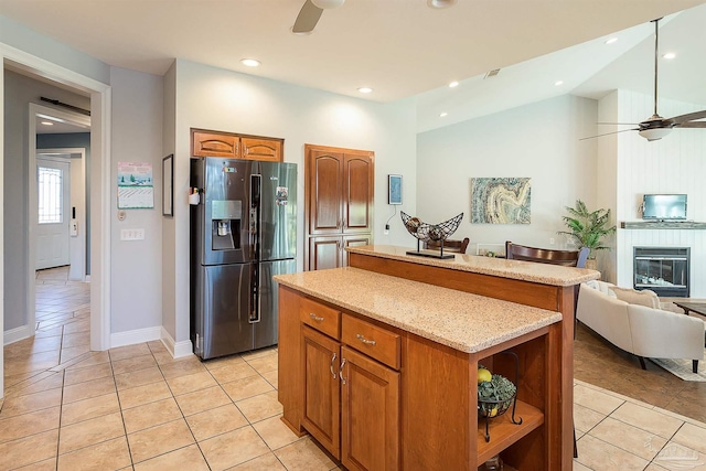 kitchen featuring light stone countertops, ceiling fan, light tile patterned floors, stainless steel fridge with ice dispenser, and a center island