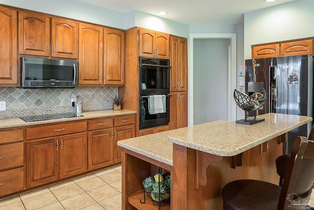 kitchen featuring tasteful backsplash, light stone counters, a breakfast bar area, light tile patterned flooring, and black appliances