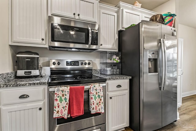 kitchen featuring hardwood / wood-style floors, stainless steel appliances, white cabinetry, and dark stone countertops