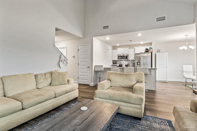 living room featuring wood-type flooring, a towering ceiling, and an inviting chandelier