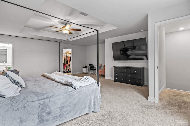 carpeted bedroom featuring ceiling fan, a closet, a spacious closet, and a tray ceiling