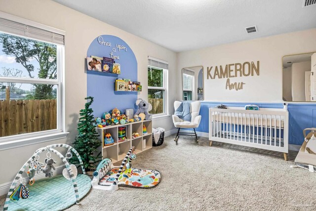 carpeted bedroom with multiple windows and a nursery area