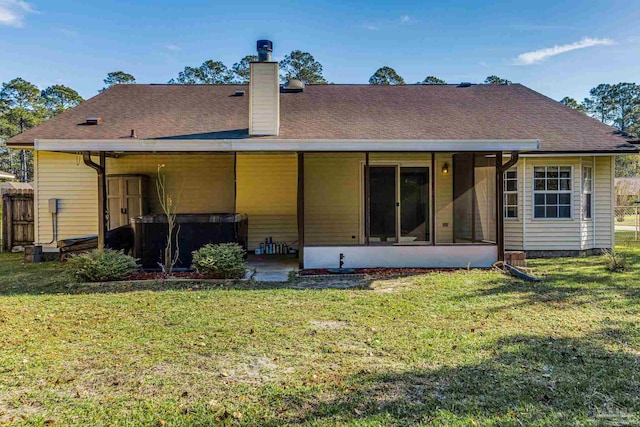 rear view of property featuring a sunroom, a hot tub, and a lawn