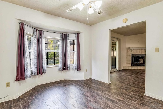 empty room featuring a textured ceiling, dark hardwood / wood-style floors, ceiling fan, and a tiled fireplace