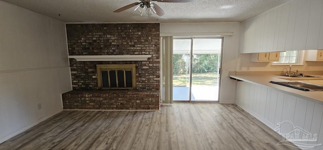 unfurnished living room with hardwood / wood-style floors, sink, a brick fireplace, ceiling fan, and a textured ceiling