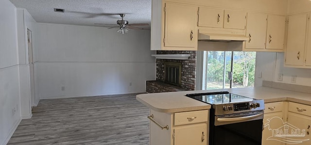 kitchen with stainless steel electric stove, ceiling fan, light wood-type flooring, a textured ceiling, and kitchen peninsula