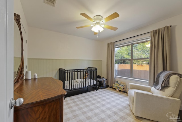 carpeted bedroom featuring a nursery area and ceiling fan