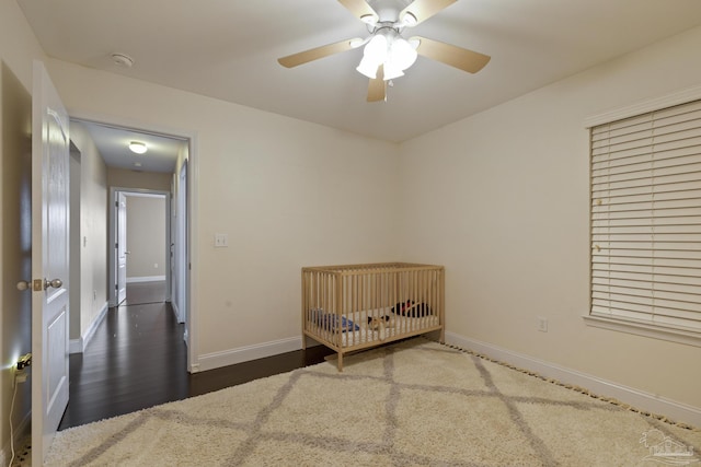 unfurnished bedroom with dark wood-type flooring, ceiling fan, and a crib
