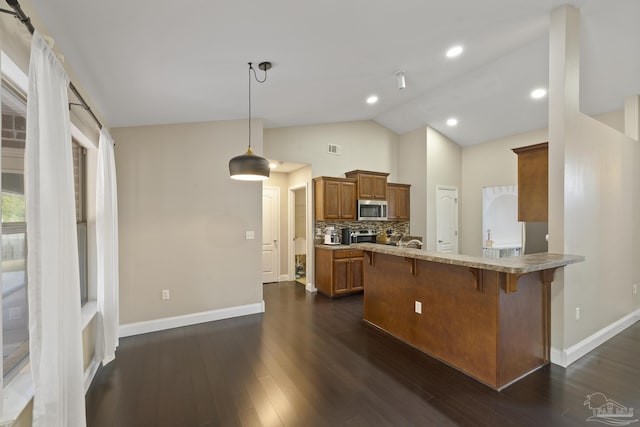 kitchen featuring a breakfast bar, tasteful backsplash, dark hardwood / wood-style flooring, vaulted ceiling, and kitchen peninsula