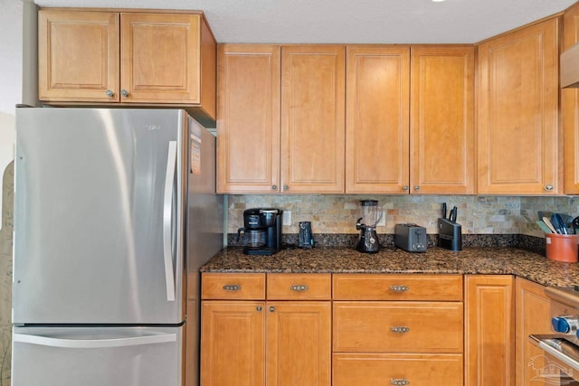 kitchen with dark stone countertops, backsplash, and stainless steel refrigerator