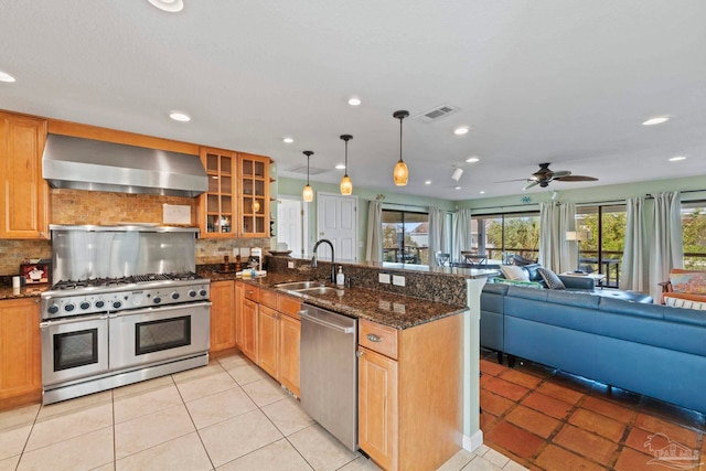 kitchen with wall chimney range hood, hanging light fixtures, stainless steel appliances, kitchen peninsula, and sink