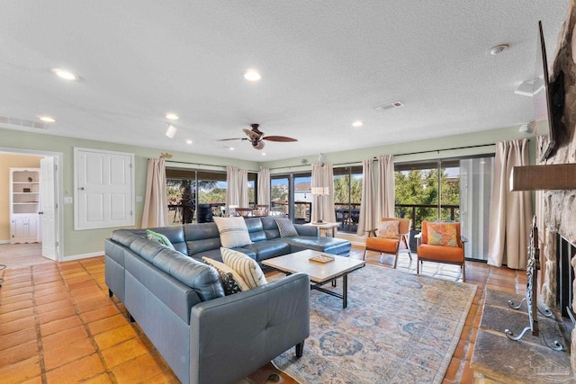 tiled living room with a stone fireplace, a textured ceiling, and ceiling fan