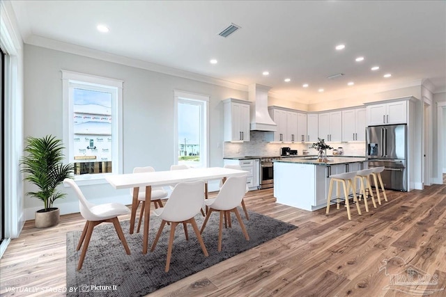 kitchen featuring light hardwood / wood-style flooring, premium range hood, appliances with stainless steel finishes, and white cabinetry