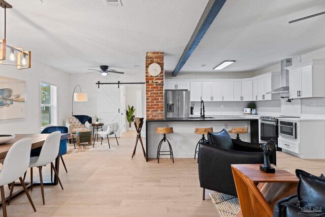 kitchen featuring stainless steel appliances, open floor plan, wall chimney range hood, and a barn door