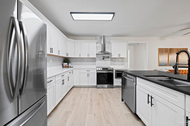 kitchen with decorative backsplash, light wood-style flooring, appliances with stainless steel finishes, wall chimney range hood, and a sink