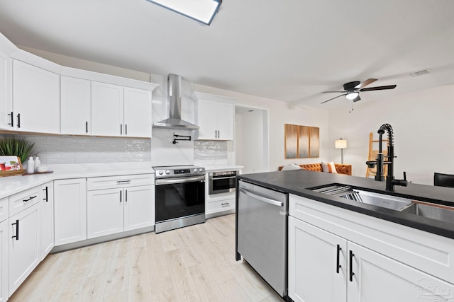 kitchen with wall chimney exhaust hood, appliances with stainless steel finishes, light wood-type flooring, white cabinetry, and a sink