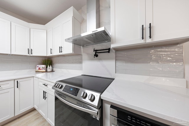 kitchen with stainless steel electric range oven, wall chimney range hood, backsplash, and white cabinetry